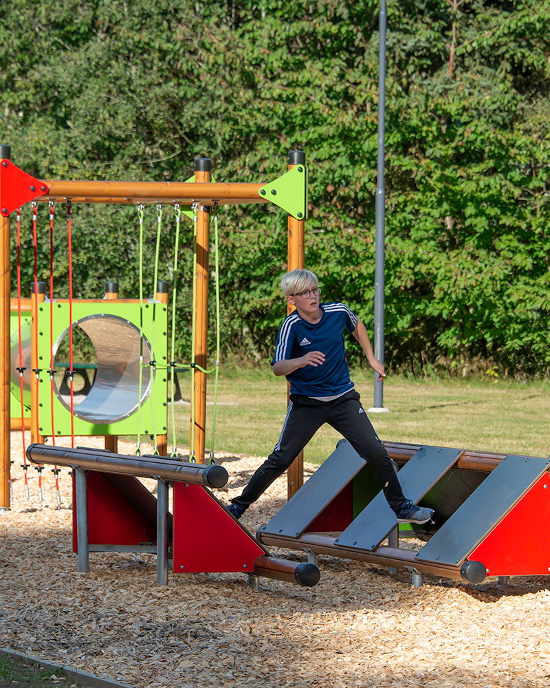 A boy is energetically making his way through a large obstacle course at a playground.